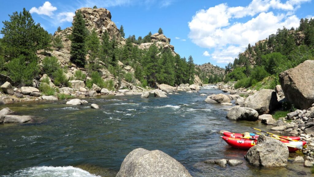 A red boat sits on the side of the Arkansas river with class II rapids