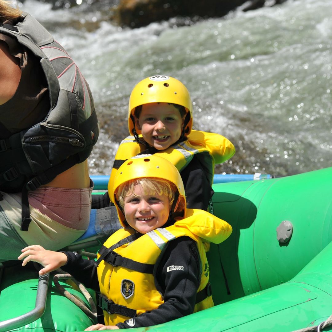 Two kids with helmets in a green raft