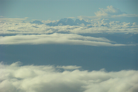 A photo taken from a plan of mountains pointing out above clouds