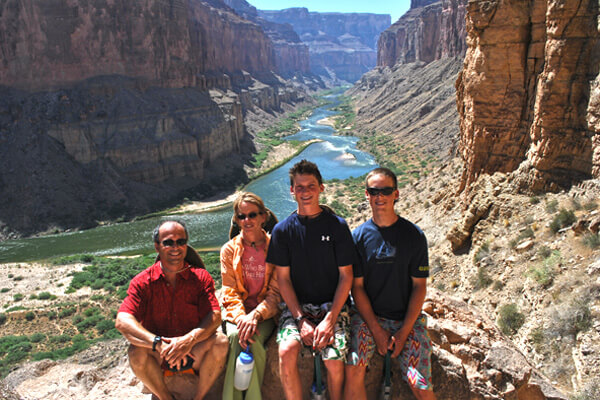 A family sits for the camera with a scenic river flowing through a canyon below