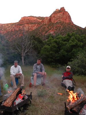 Men site around two fire as the sun sets of a red rock formation