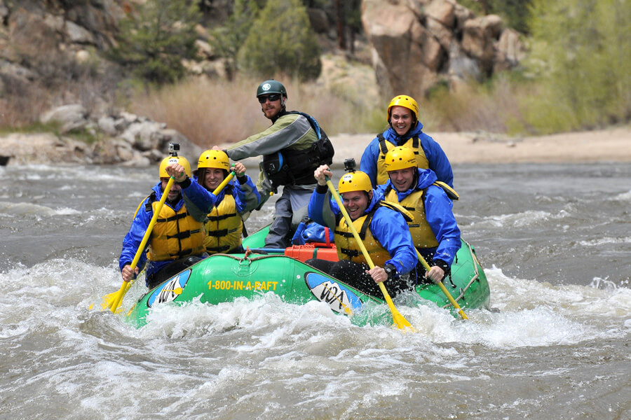 A group of people in a green raft paddle down a river