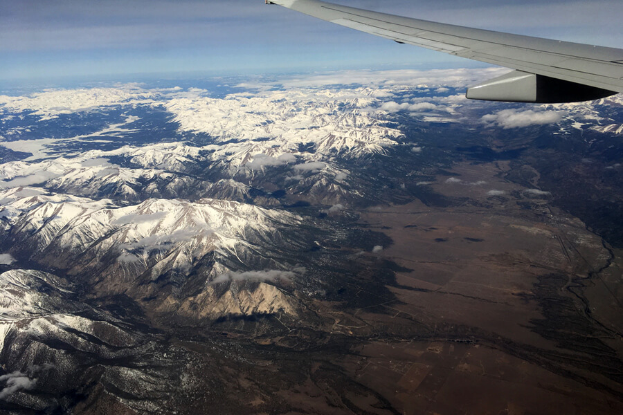 A photo from inside a plane of snow covered peaks
