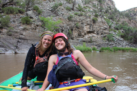 Two women smile from inside a raft with a rocks in the background