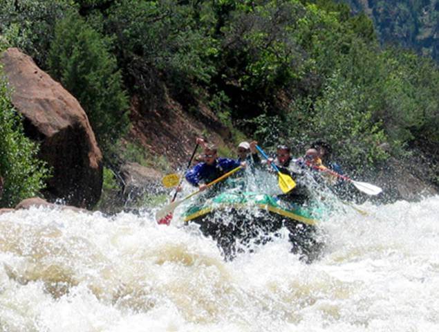 Passengers on a green boat paddle through extreme white water