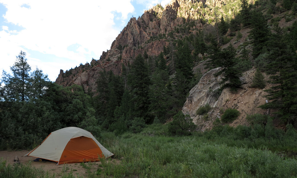 an orange tent pitched in front of a canyon wall