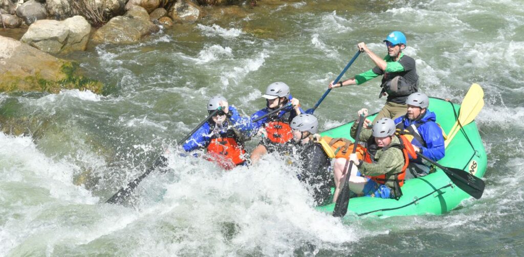 People on a green raft paddle hard through rapids