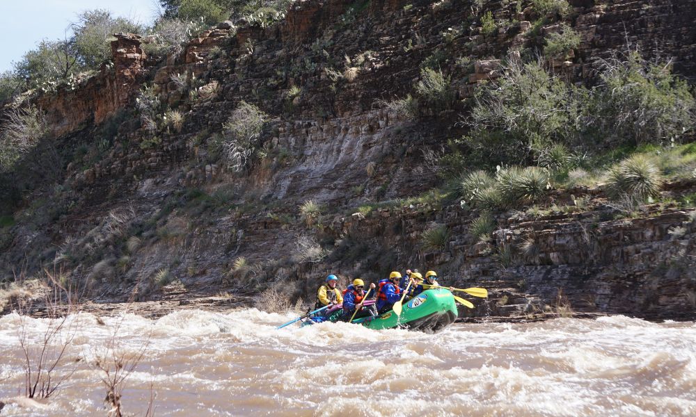A green boat of rafters paddles down Arizona's salt river